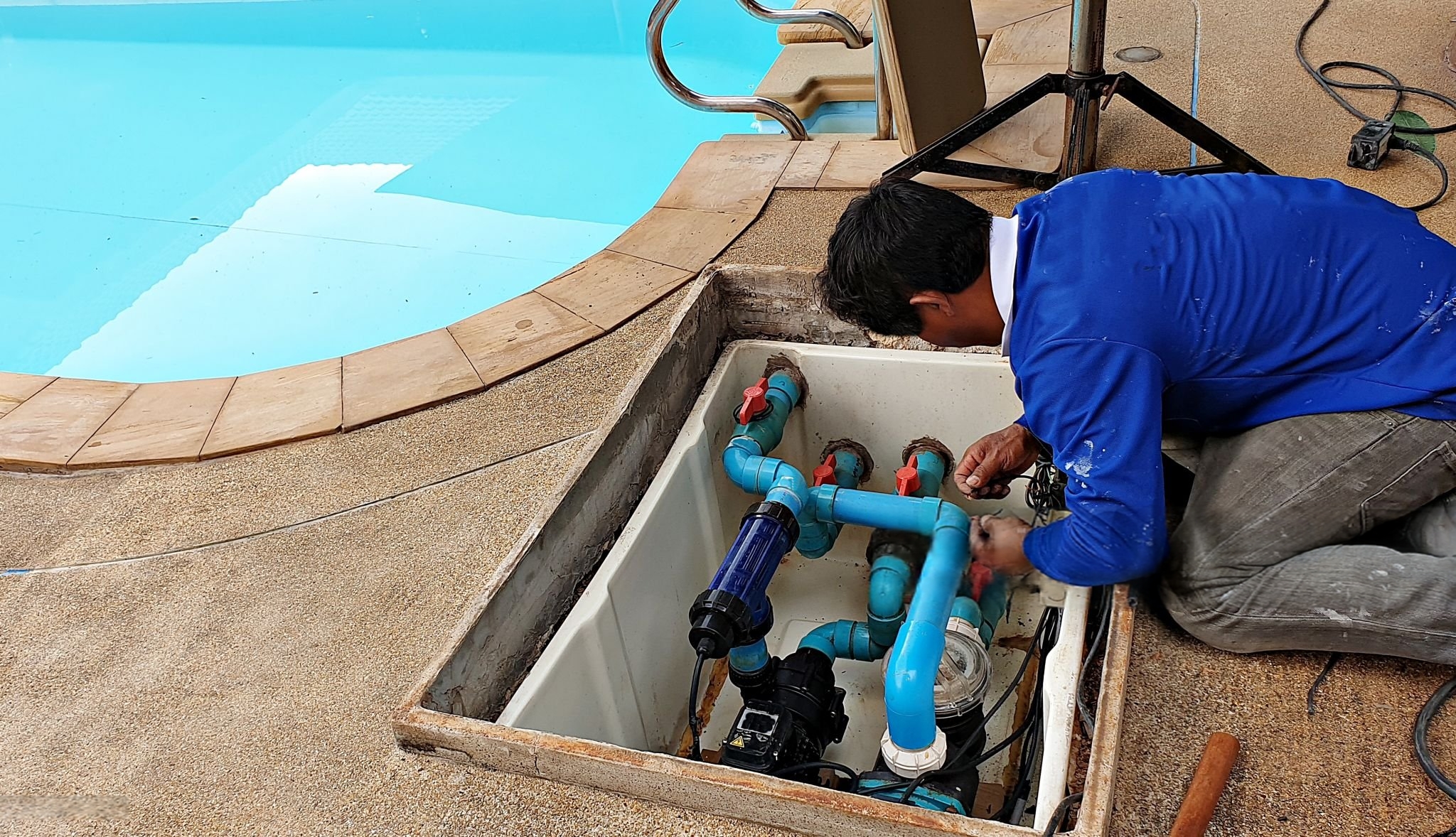 Pool technician working on underground plumbing and pump equipment near poolside