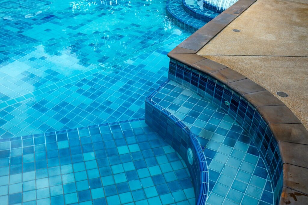 Close-up of a remodeled swimming pool with raised spa, tile steps, and waterfall feature